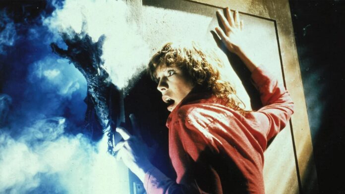 Jamie Lee Curtis leans against a door trying to keep an ominous hand from getting inside in The Fog (1980)