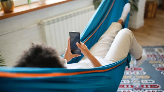 A person lounges in a hammock with a phone in their hands.