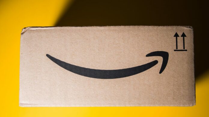 a side view of an old Amazon delivery box against a bright yellow background. the top left corner is covered in shade from the box&apos;s shadow