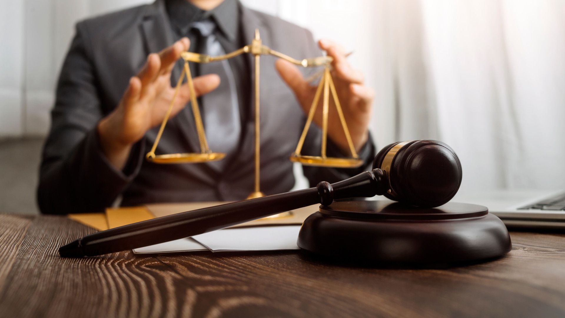 Person in suit behind a court gavel and some old scales