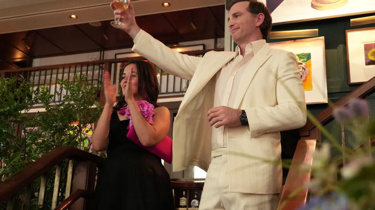 Joe Gebbia, dressed in a cream-colored suit, raises a glass of wine in a toasting gesture.