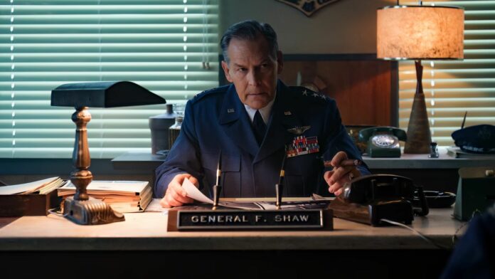 James Remar as General Shaw, sitting at his desk in uniform and smoking a cigar
