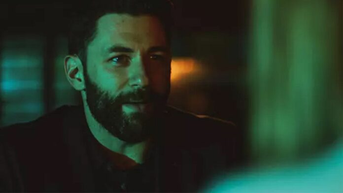 A man with a beard and black collared shirt smiles 