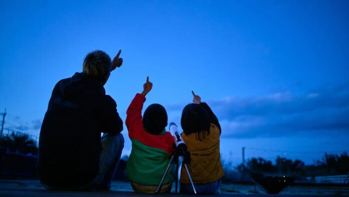 Family is seen sitting outside looking up at the sky