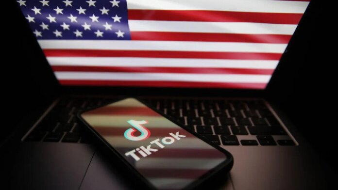 A US flag is reflected in the screen of a smartphone displaying the TikTok app logo.
