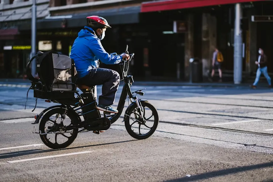 Delivery rider on e-bike navigating a shared urban cycle path, representing the economic impact of e-bike enforcement on lower-income workers