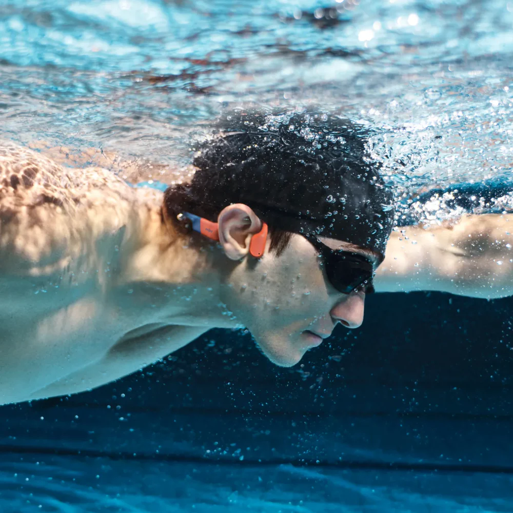 Swimmer wearing Shokz OpenSwim Pro headphones in a pool with swim goggles